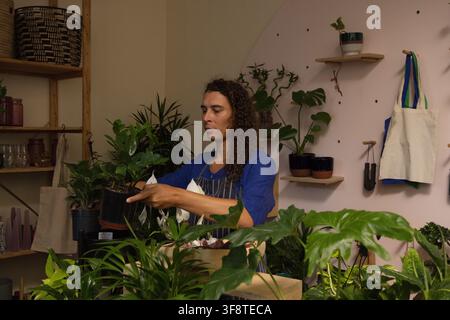 African American non-binary plant shop worker inspecting small black nursery pot at potting bench Stock Photo