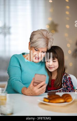 Grandmother and granddaughter bonding using smartphone during Christmas holiday Stock Photo