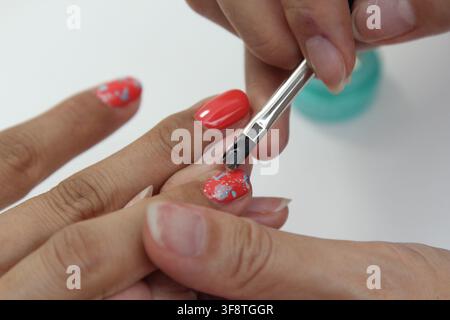 Nail technician applying nail art with a fine brush on a client's fingernails in a beauty salon, showcasing professional manicure service. Stock Photo