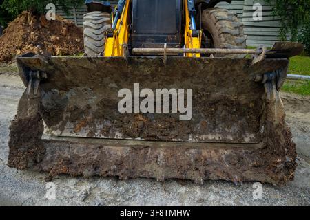 Close up of large heavy yellow excavator front steel bucket covered in wet brown dirt. Concept: heavy machinery power Stock Photo