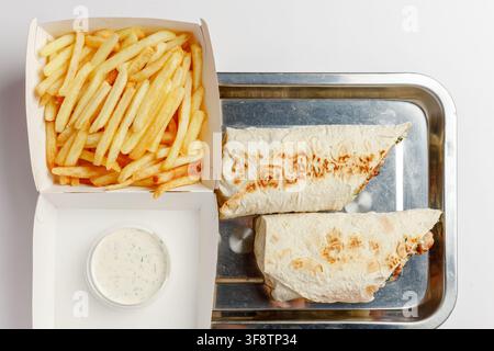 Two halves of chicken shawarma on metal tray with french fries and garlic dip Stock Photo