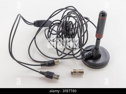 A small black TV antenna with tangled cables sits on a white background Stock Photo