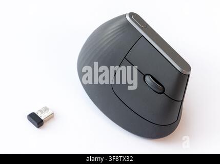 A dark gray ergonomic wireless mouse and its USB receiver on white Stock Photo