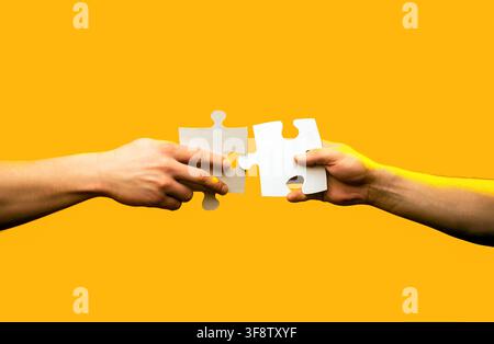 Male and female hand joining two matching puzzle pieces together in a conceptual image of teamwork and cooperation. Hands connecting puzzle pieces. Stock Photo