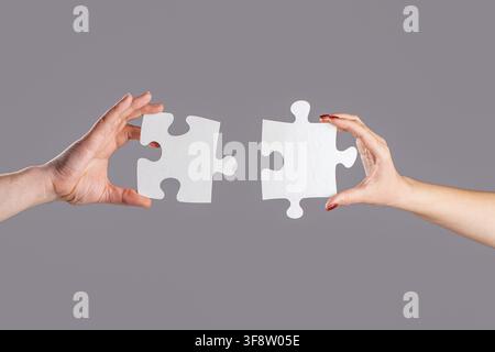 Hands connecting puzzle. Hand of the man and hand of woman fold puzzle, closeup. Puzzles. Man and woman holds in hand a jigsaw puzzle. Business Stock Photo