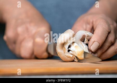 Chef cutting, slicing mushrooms champignon closeup. Hands cooking healthy vegetables. Hands of man cutting mushrooms with knife in kitchen. Woman Stock Photo