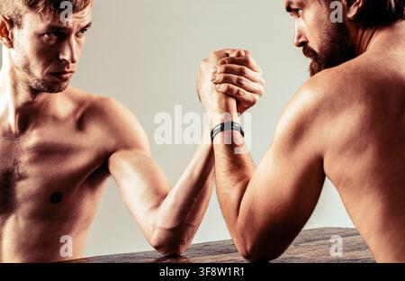 Arms wrestling thin hand, big strong arm. Strong and weak, unequal match. Heavily muscled bearded man arm wrestling a puny weak man Stock Photo