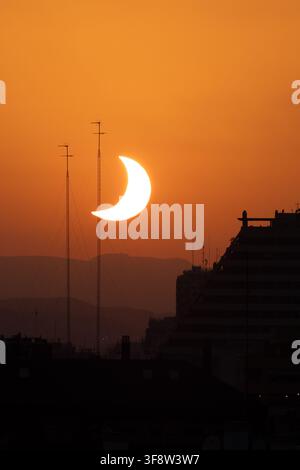 Crescent sun in orange sky above urban rooftops Stock Photo