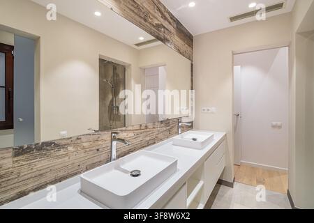 Modern minimalist bathroom interior with dual white vessel sinks wooden accents and large mirror under bright recessed lighting Stock Photo