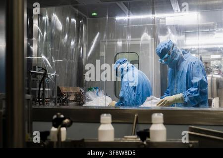 Lab workers wearing protective hazmat suits working in sterile cleanroom at pharmaceutical plant Stock Photo