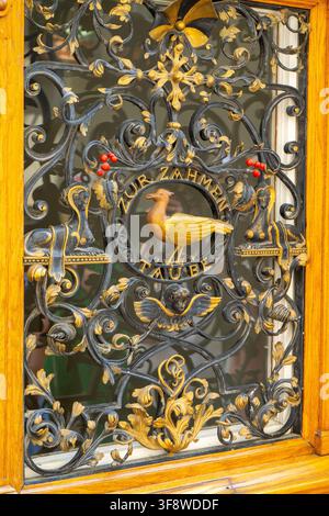 Ornate Wrought Iron Gate with Golden Dove Emblem, Decorative Flourishes and Inscription in Zurich. Wooden Entrance Door with Grille in Old Town. Zurich, Switzerland - June 23, 2026 Stock Photo