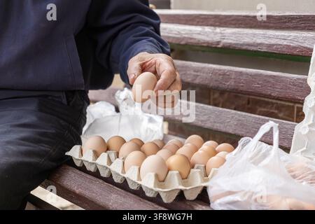 A mature person selects natural brown eggs from a full paper tray outdoors, showcasing fresh food quality and the farm-to-table lifestyle with wholeso Stock Photo