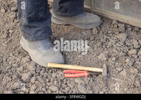 Sturdy work boots resting on dark rough ground near essential hand tools, emphasizing professional maintenance, farm utility, home repair, and constru Stock Photo