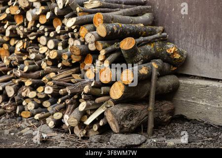 Stacked firewood arranged in a dense heap by a stone building for heating purposes, representing rural warmth, rustic energy preparation, and traditio Stock Photo
