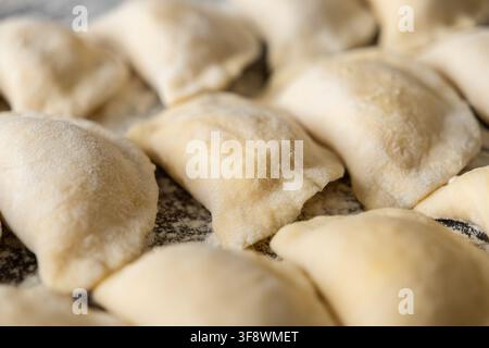 Uncooked dough dumplings laid out on a dusty kitchen table, highlighting the texture of pastry and flour during the careful preparation of classic com Stock Photo