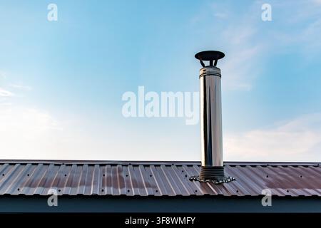 Stainless steel chimney pipe on corrugated metal rooftop against sky Stock Photo