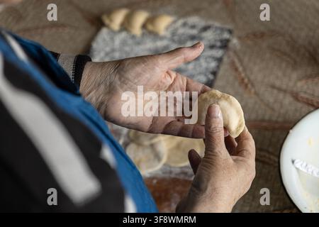 Close hands of an older woman folding dough to create savory dumplings, emphasizing handmade quality, cultural culinary heritage, and the nourishing s Stock Photo