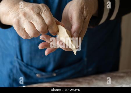 Artisan hands crimping a homemade dumpling to seal the filling inside, highlighting careful culinary craftsmanship and heritage cooking methods for pr Stock Photo