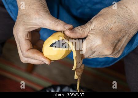 Close up of an older person skinning a rustic potato using a sharp blade, capturing the simple process of meal creation and everyday rural kitchen cho Stock Photo