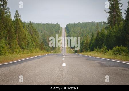 Straight asphalt road climbing steeply through dense coniferous forest in Siberia, Russia Stock Photo