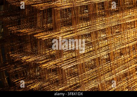 Detailed close-up of stacked metal mesh panels showcasing a rusty patina. Warm lighting highlights the texture and geometric grid structure of the mat Stock Photo