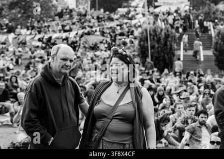 HAPPY COUPLE IN CROWD AT GREEN MAN FESTIVAL, REPORTAGE, GREEN MAN FESTIVAL 2016, BRECON, WALES, UK, 2016: A smiling woman with glitter on her face and a festive headband stands next to a man in a hoodie within a large festival crowd in this black and white photograph. Photo: Rob Watkins. INFO: The Green Man Festival began in 2003 in Wales. Held annually in the Brecon Beacons on August’s third weekend, it celebrates alternative music, arts, literature, science and family-friendly culture in a beautiful mountain setting. Stock Photo