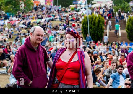 COLOURFUL COUPLE AT GREEN MAN MUSIC FESTIVAL, REPORTAGE, GREEN MAN FESTIVAL 2016, BRECON, WALES, UK, 2016: A woman with red hair, a red top, and a colorful headband smiles next to a man in a purple hoodie, standing in a large crowd at an outdoor festival. Photo: Rob Watkins. INFO: The Green Man Festival began in 2003 in Wales. Held annually in the Brecon Beacons on August’s third weekend, it celebrates alternative music, arts, literature, science and family-friendly culture in a beautiful mountain setting. Stock Photo