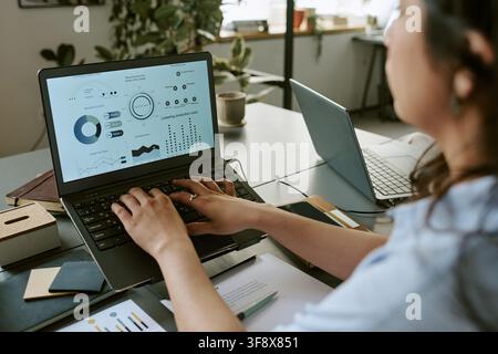 Woman Analyzing Financial Data on Laptop in Modern Office Stock Photo