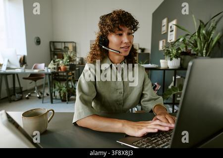 Biracial Woman Wearing Headset Typing on Laptop in Call Center Stock Photo
