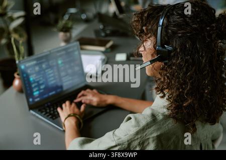 Woman Wearing Headset Typing on Laptop in Call Center Stock Photo
