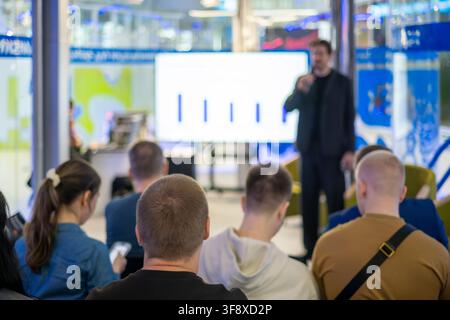 Speaker presents a bar chart on a large screen while audience members follow the talk from their seats. Stock Photo