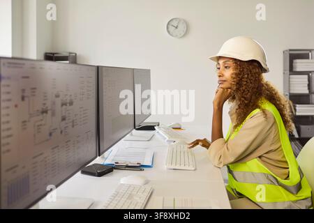 Female engineer monitoring industrial systems on multiple screens in control room Stock Photo