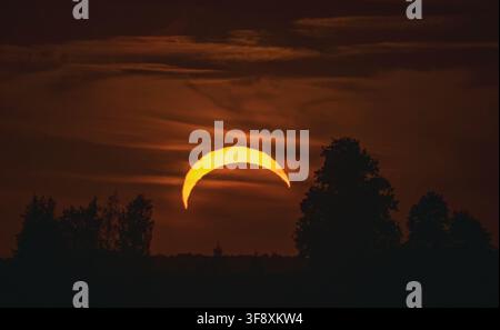 Orange crescent sun during partial solar eclipse in dark sky in Lithuania Stock Photo