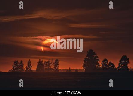 Orange crescent sun during partial solar eclipse in dark sky in Lithuania Stock Photo