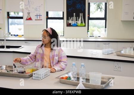 Youth female student wearing pastel plaid shirt and goggles using dropper over test tubes in lab Stock Photo