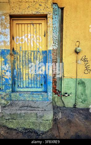Colorful weathered doorway with peeling paint graffiti and utility meter on textured urban wall Stock Photo