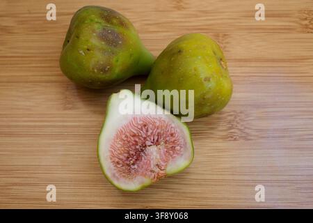 Fresh green figs arranged on a wooden table, including a halved fig revealing its delicate pink flesh and seeds. Natural fruit still life highlighting Stock Photo