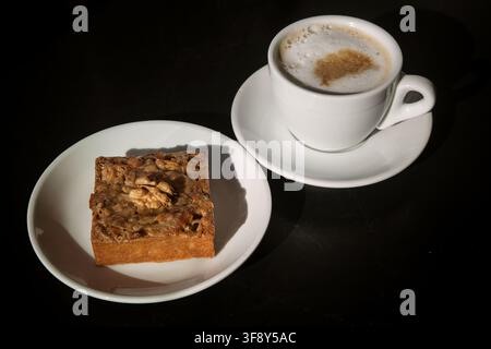walnut cake on a white plate next to a Cup of cappuccino, Sunny photo. Stock Photo