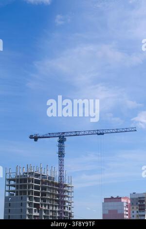 A bustling construction site featuring a tall crane amidst the backdrop of a clear blue sky. The unfinished skyscraper stands prominently, showcasing Stock Photo