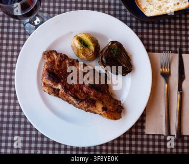Grilled beef ribs served on plate with side dish of boiled potatoes and baked artichokes. Popular Spanish combination meal Stock Photo