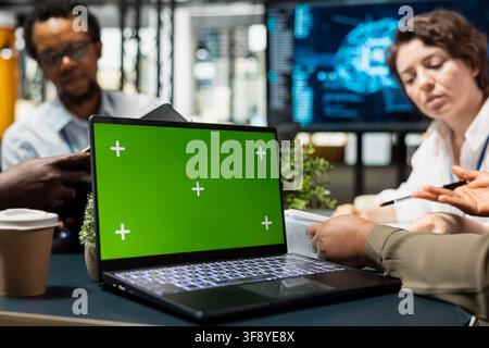 Green screen laptop next to IT employees implementing AI solutions to increase productivity. Close up of mockup notebook and engineers discussing software development roadmap in startup office Stock Photo