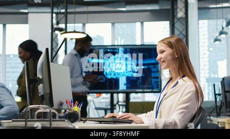 Manager supervising young trainee in office using AI technology, monitoring performance dashboards. Team leader overseeing work done by junior dev tuning neural networks using tools on PC, camera A Stock Photo