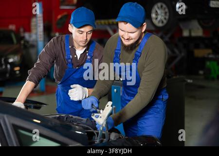 Two professional auto mechanics repairing broken car together in car service center Stock Photo
