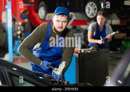 Professional mechanic man in uniform repairing car in auto repair garage Stock Photo