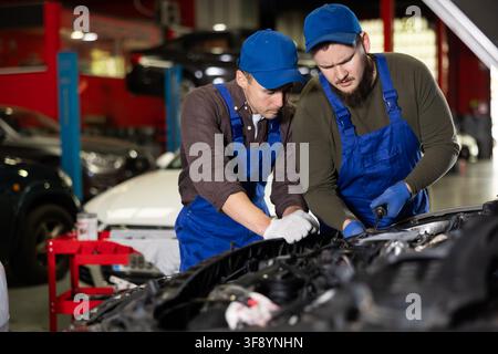 Two professional auto mechanics repairing broken car together in car service center Stock Photo