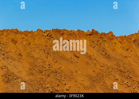 Large heaps of raw soil and dirt piled up at a construction site against a clear blue sky, textured mounds of earth showing excavation progress in bri Stock Photo