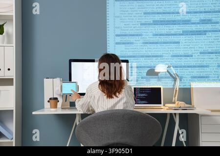Female programmer working on multiple screens with code displayed, software development and technology Stock Photo