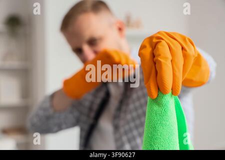 Man in orange rubber gloves holding a green microfiber cleaning cloth, home hygiene and sanitation concept, Essential tools for domestic cleaning and Stock Photo