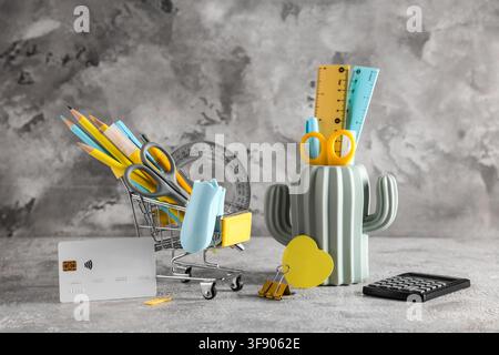 Back to school shopping with miniature cart full of stationery and credit card on a gray background, a credit card is placed next to the cart, payment Stock Photo