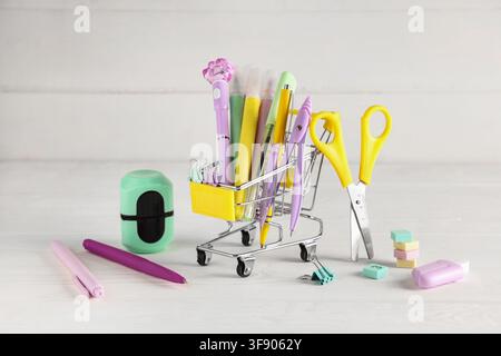 Miniature shopping cart filled with colorful school and office supplies on a white wooden background Stock Photo